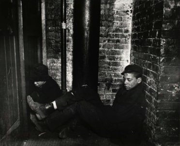 Archival black and white historical photograph of children sitting by a brick wall.