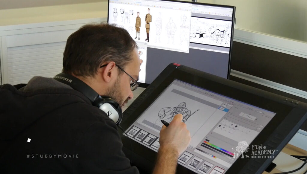 An animator working at a desk, drawing character designs on a digital pen display tablet.